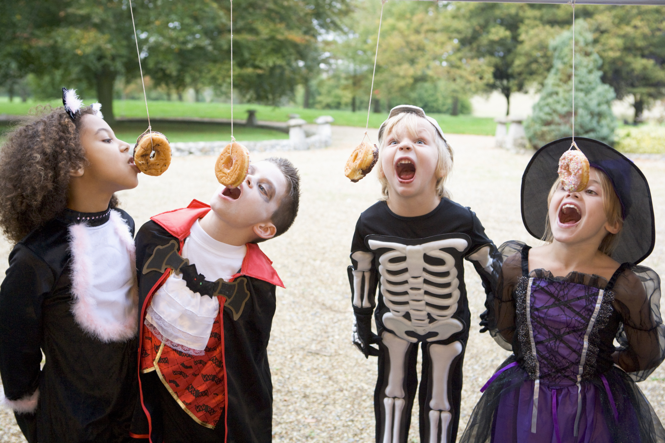 Four young friends on Halloween in costumes eating donuts hanging off strings.