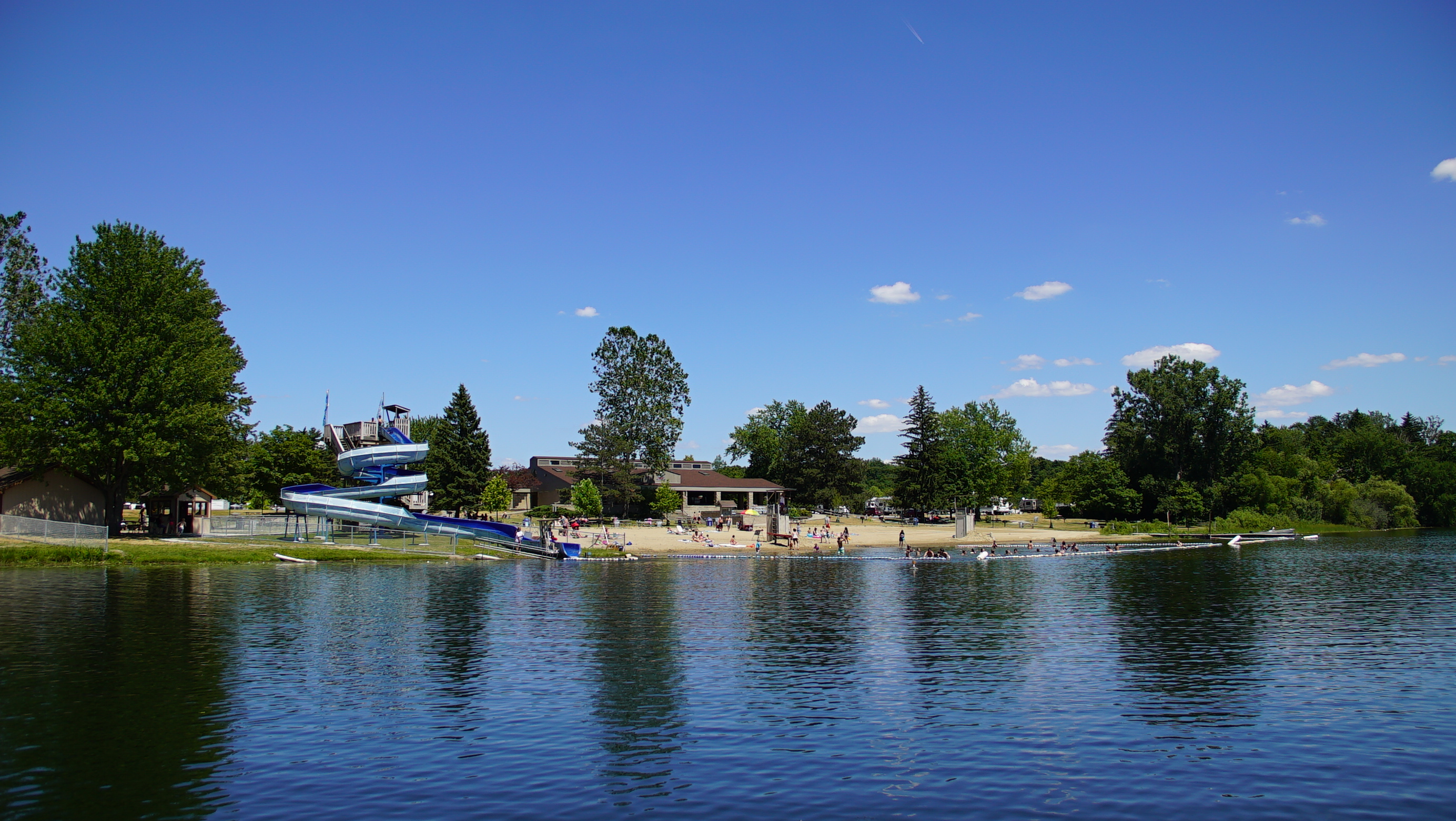A lake with a waterslide and beach on the opposite shore.