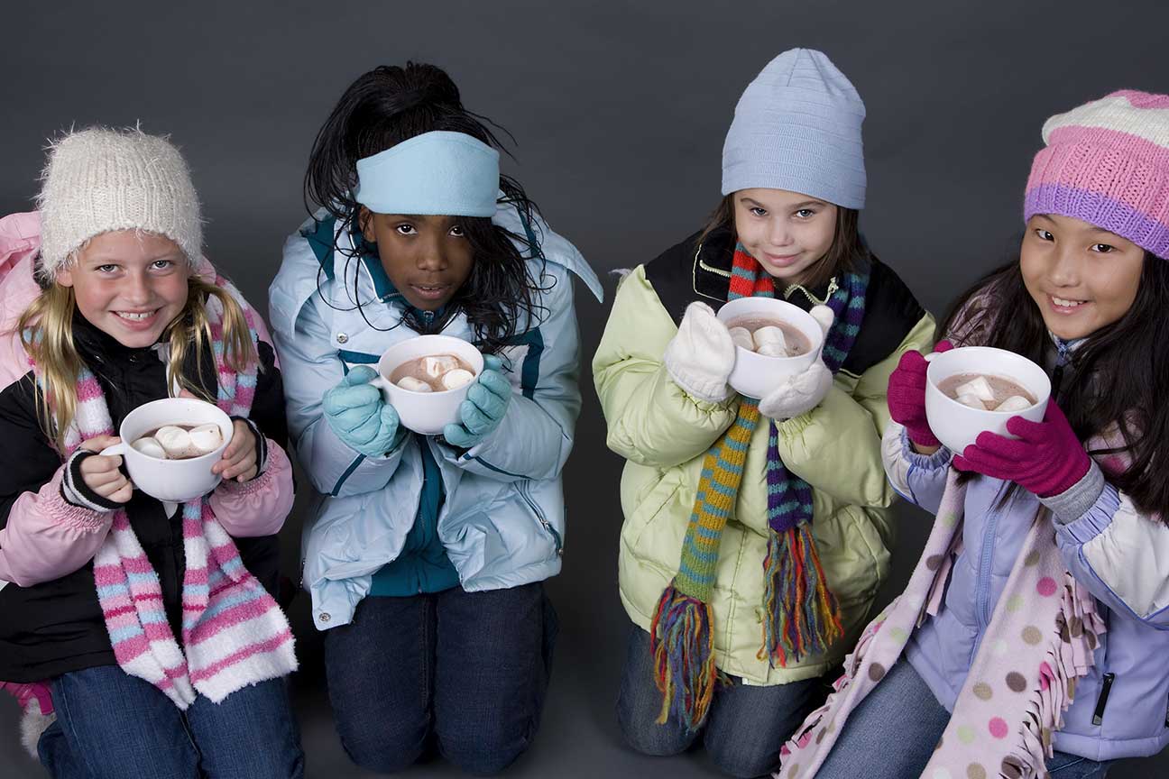 Four young girls bundled up in winter coats drinking hot chocolate.