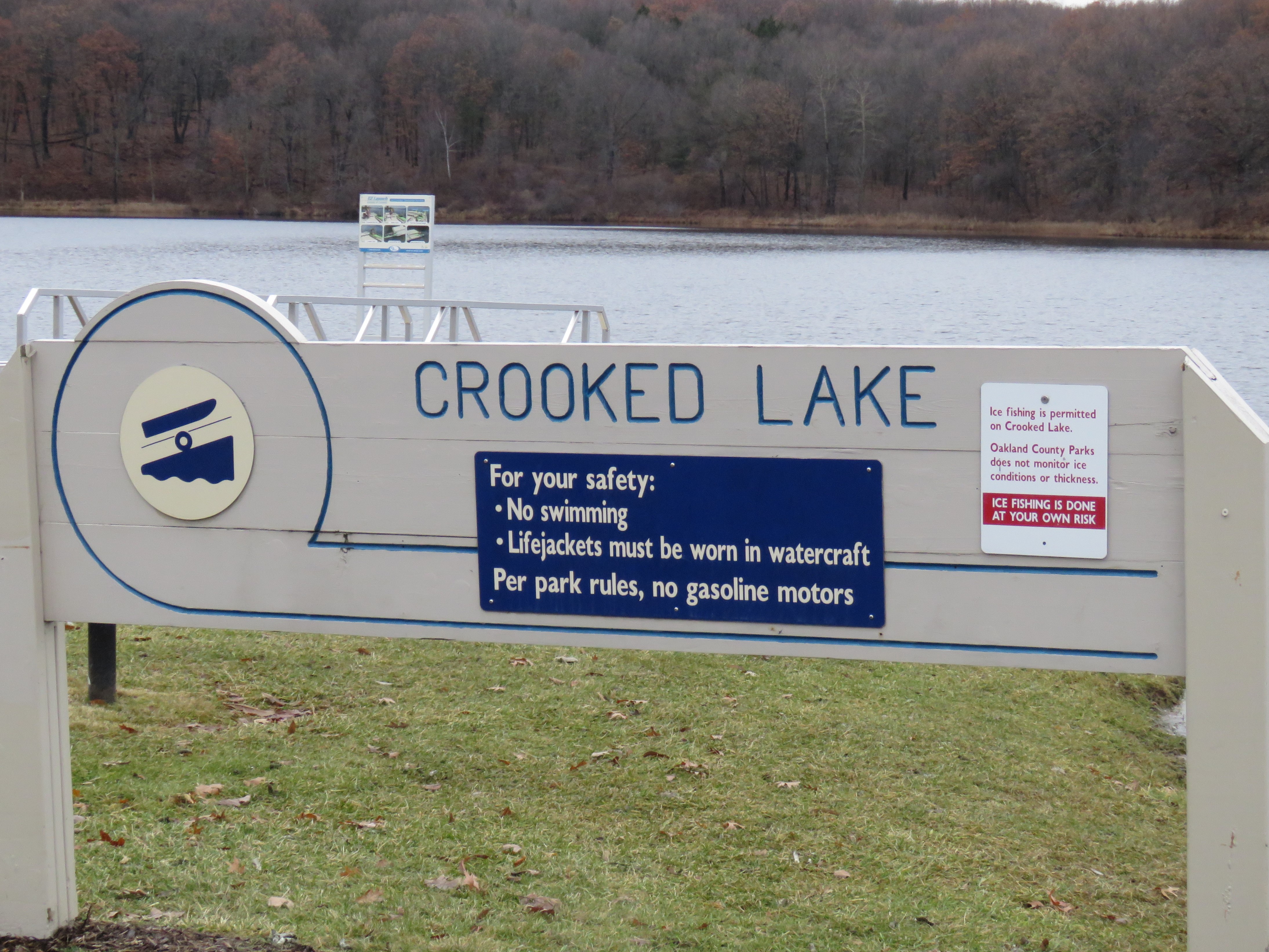 A lake with a gray sign in front of it that reads: Crooked Lake.