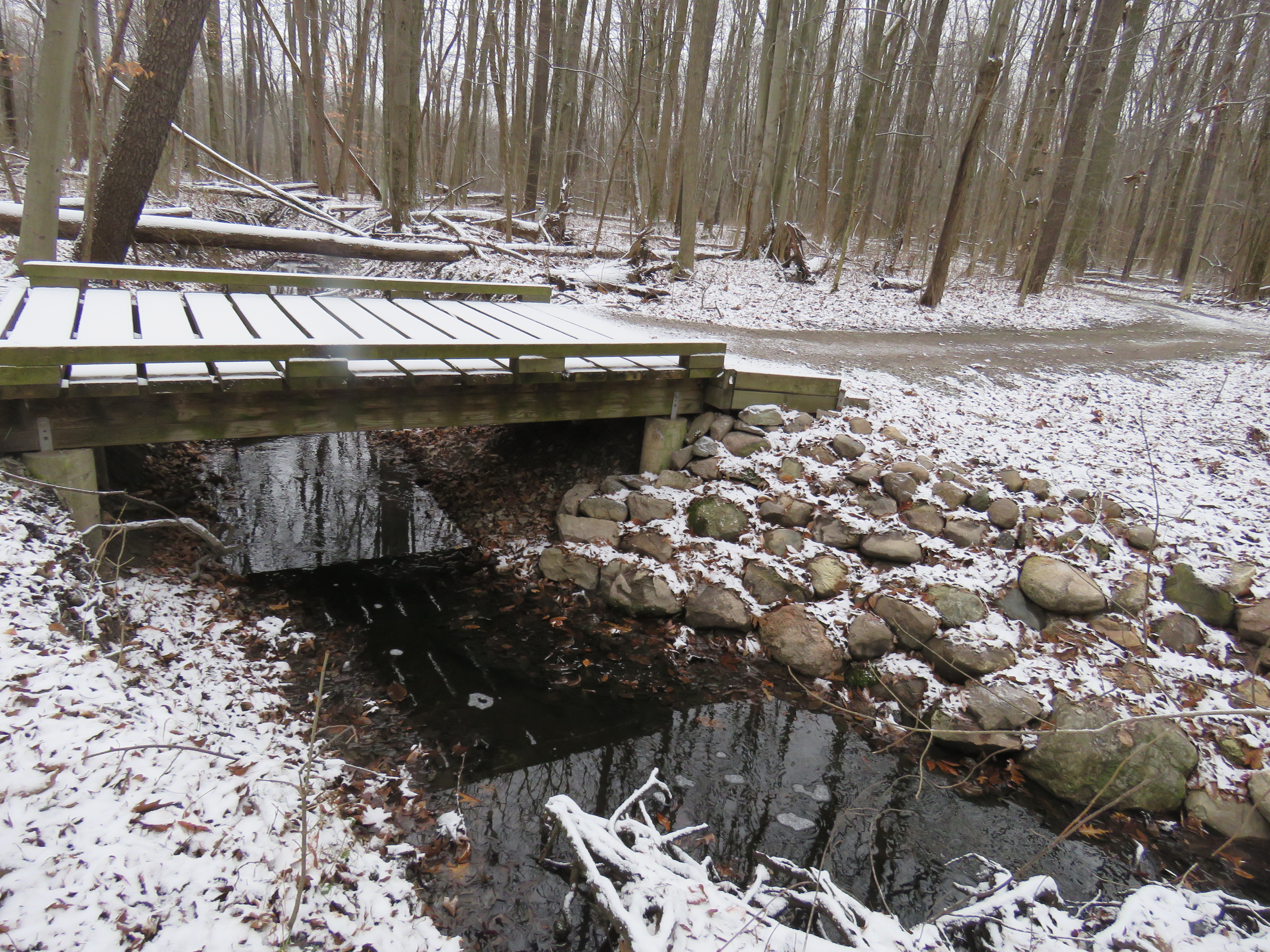 A snow covered wooden bridge over a creek