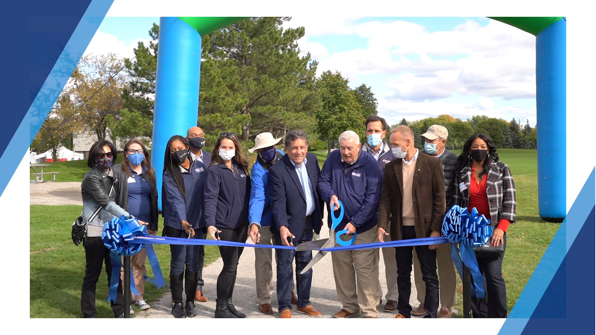 A large group of people gathered as a blue ribbon is cut with giant scissors