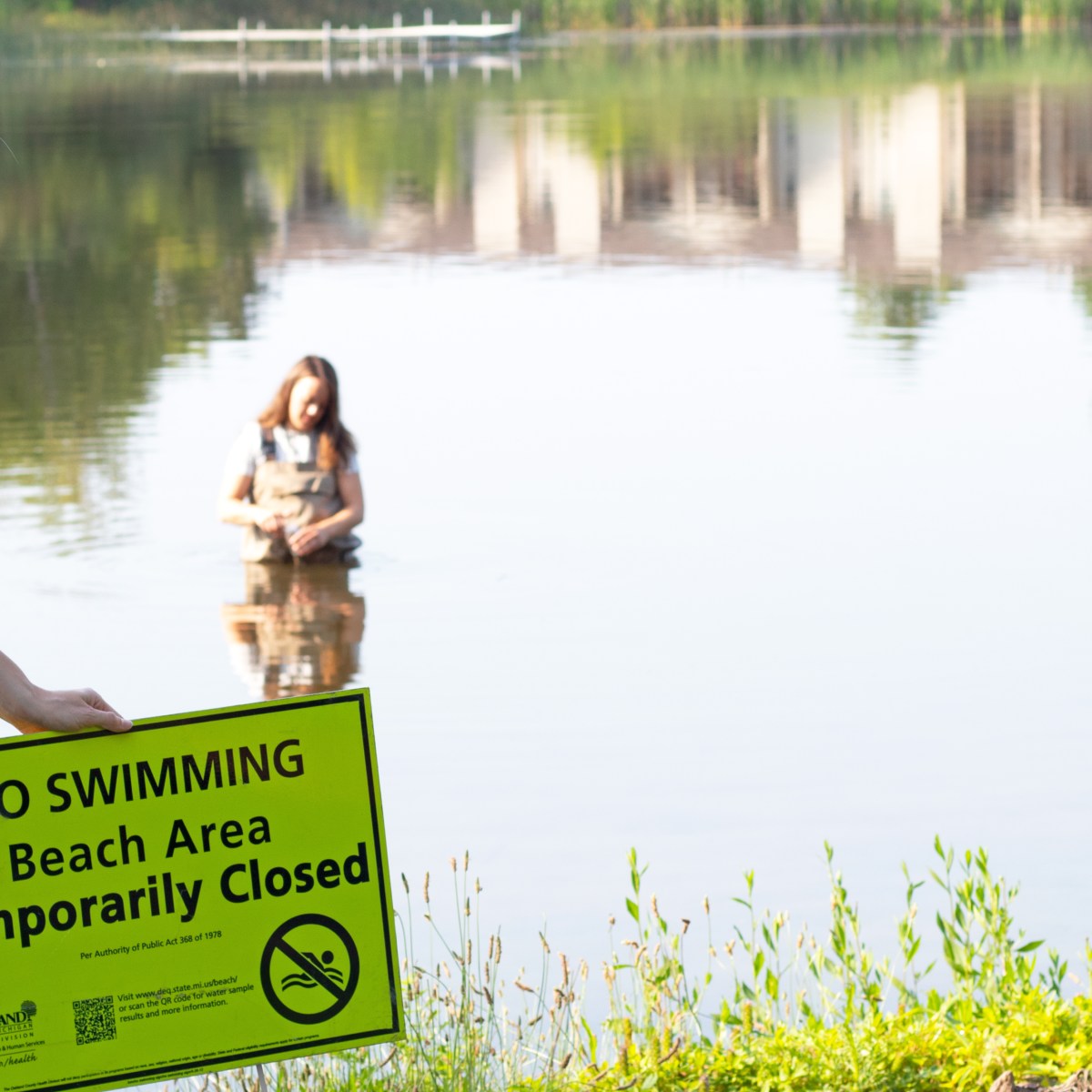 Lake with sign in ground that says "no swimming beach area temporarily closed"