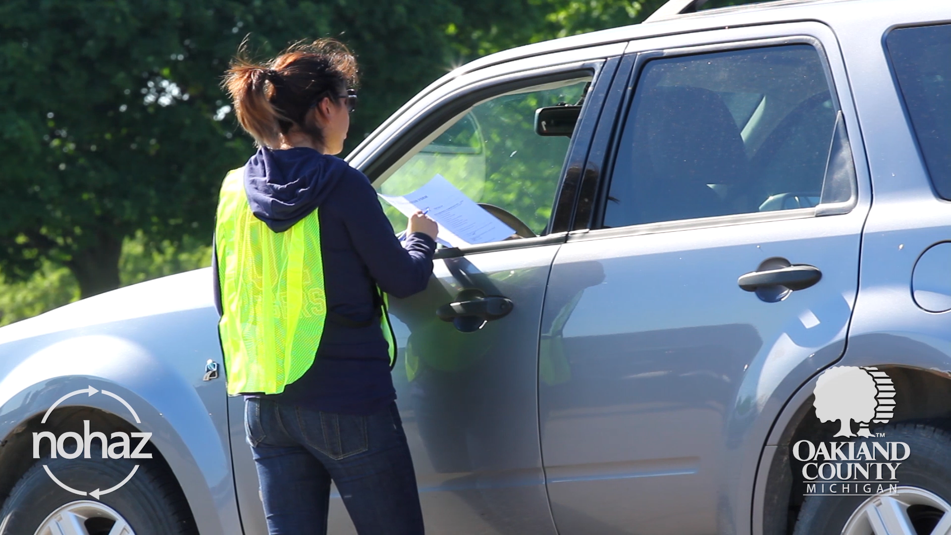 Woman wearing safety vest talking to person through car window at NoHaz event