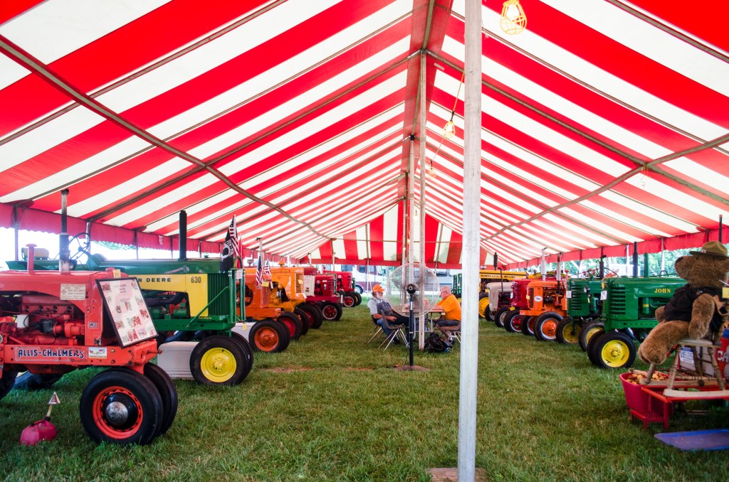 Old tractors lined up underneath tent at Oakland County Fair