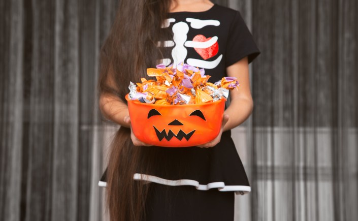 Little girl is holding a scary bowl with candies She dressed in Halloween skeleton costume
