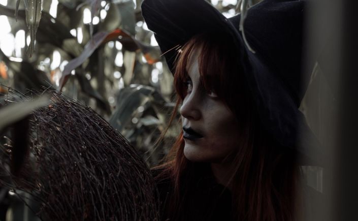 Woman dressed as witch in a cornfield.